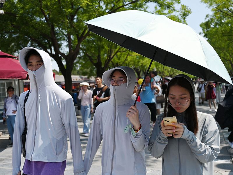 Đối mặt với thời tiết nắng nóng khắc nghiệt, người dân Trung Quốc mặc áo chống nắng kín mít, che ô khi đến thăm Tử Cấm Thành ở Bắc Kinh - Ảnh: AFP