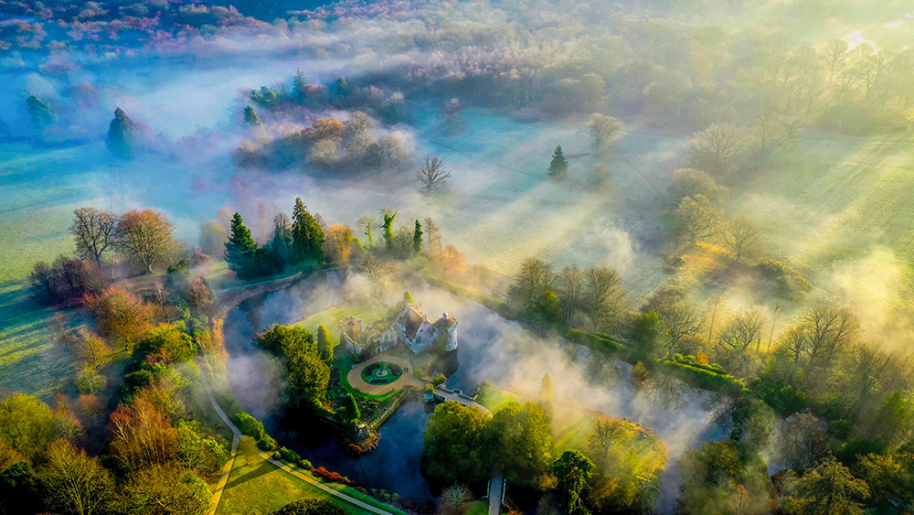Sương mù huyền ảo xen lẫn những tia nắng chiếu xuống khu vực quanh tòa lâu đài cổ Scotney ở Kent, Vương quốc Anh trong một buổi sáng sớm. Ảnh: Chris Brown.